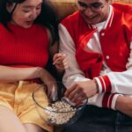 A happy couple relaxing together on a couch, sharing a bowl of popcorn indoors.